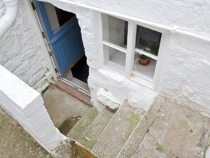 A white building with a blue door and a window with a potted plant. - Sharrowhead Cottage - E4044 (Robin Hood’s Bay)