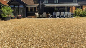 A house with a gravel driveway, a covered patio with outdoor seating, and potted plants.