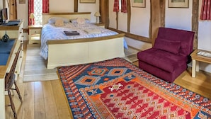 A bedroom with a large bed, a wooden ceiling, a red chair, and a patterned rug.