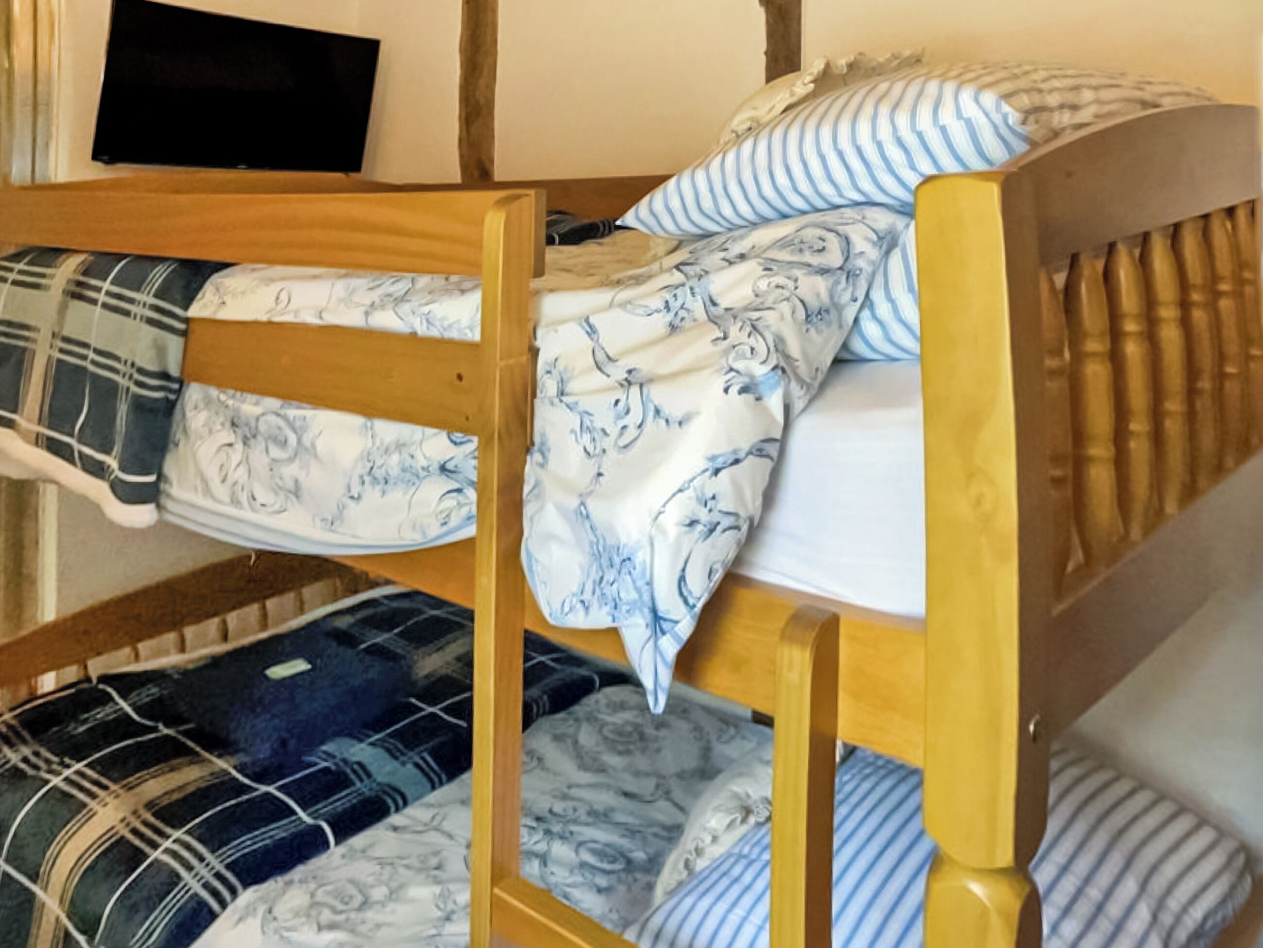 Una cama individual con estructura de madera, ropa de cama con estampado azul y blanco, y un televisor montado en la pared de arriba.