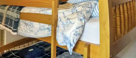 Una cama individual con estructura de madera, ropa de cama con estampado azul y blanco, y un televisor montado en la pared de arriba.