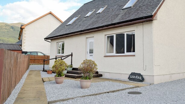 Une maison à deux étages avec un toit en pente, une clôture en bois et une allée gravillonnée.
