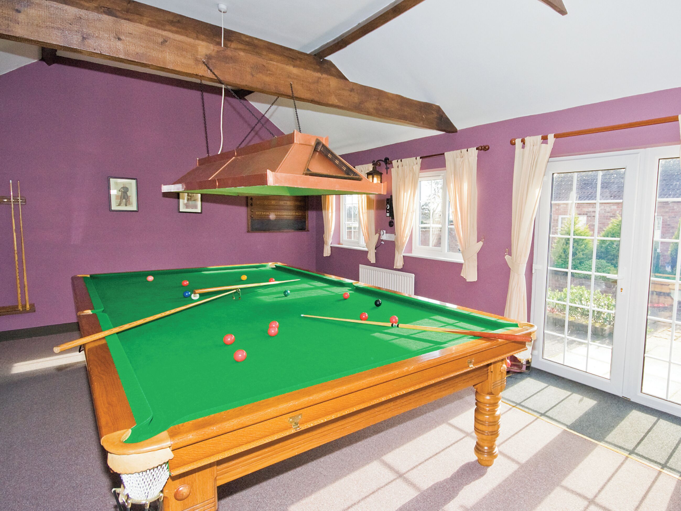 A pool table with balls, a wooden ceiling, purple walls, and a window with curtains.