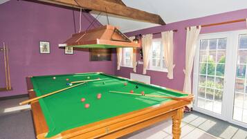 A pool table with balls, a wooden ceiling, purple walls, and a window with curtains.
