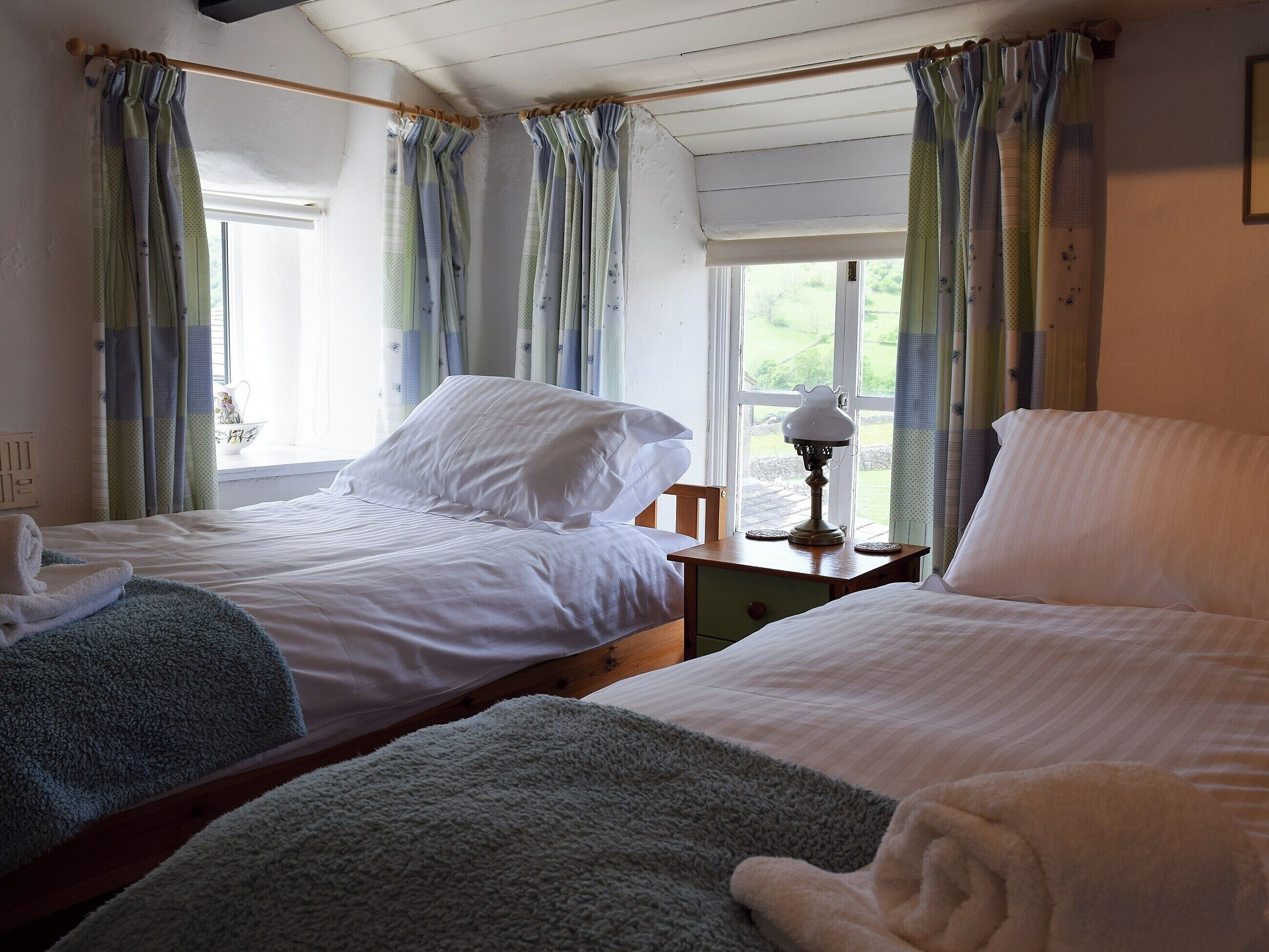 Une chambre avec deux lits, une table de chevet avec une lampe et une fenêtre avec des rideaux.