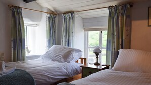 A bedroom with two beds, a bedside table with a lamp, and a window with curtains. - 2 bedroom accommodation in Starbotton, near Skipton (Starbotton, near Skipton)
