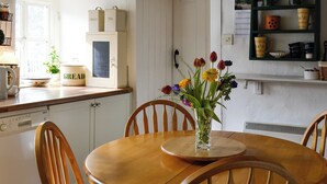 A kitchen with a wooden table, chairs, a vase with flowers, and a shelf with kitchenware. - 2 bedroom accommodation in Starbotton, near Skipton (Starbotton, near Skipton)