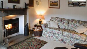 A cozy living room with a fireplace, a floral sofa, and a bookshelf with books. - 2 bedroom accommodation in Starbotton, near Skipton (Starbotton, near Skipton)