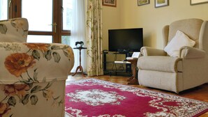 A living room with a floral armchair, a beige armchair, a television, and a red patterned rug. - 2 bedroom accommodation in Abergavenny (Abergavenny)