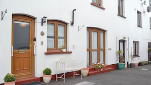 A white building with a wooden door, a bench, and potted plants. - 2 bedroom accommodation in Abergavenny (Abergavenny)