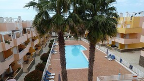 A rooftop pool area with palm trees, lounge chairs, and a clear blue pool.