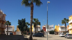A street with palm trees, parked cars, and buildings with balconies.