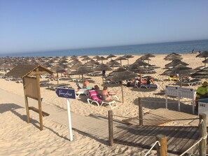 A beach with multiple sun loungers and umbrellas, a wooden structure labeled 'Paradise Beach', and a wooden boardwalk leading to the beach.