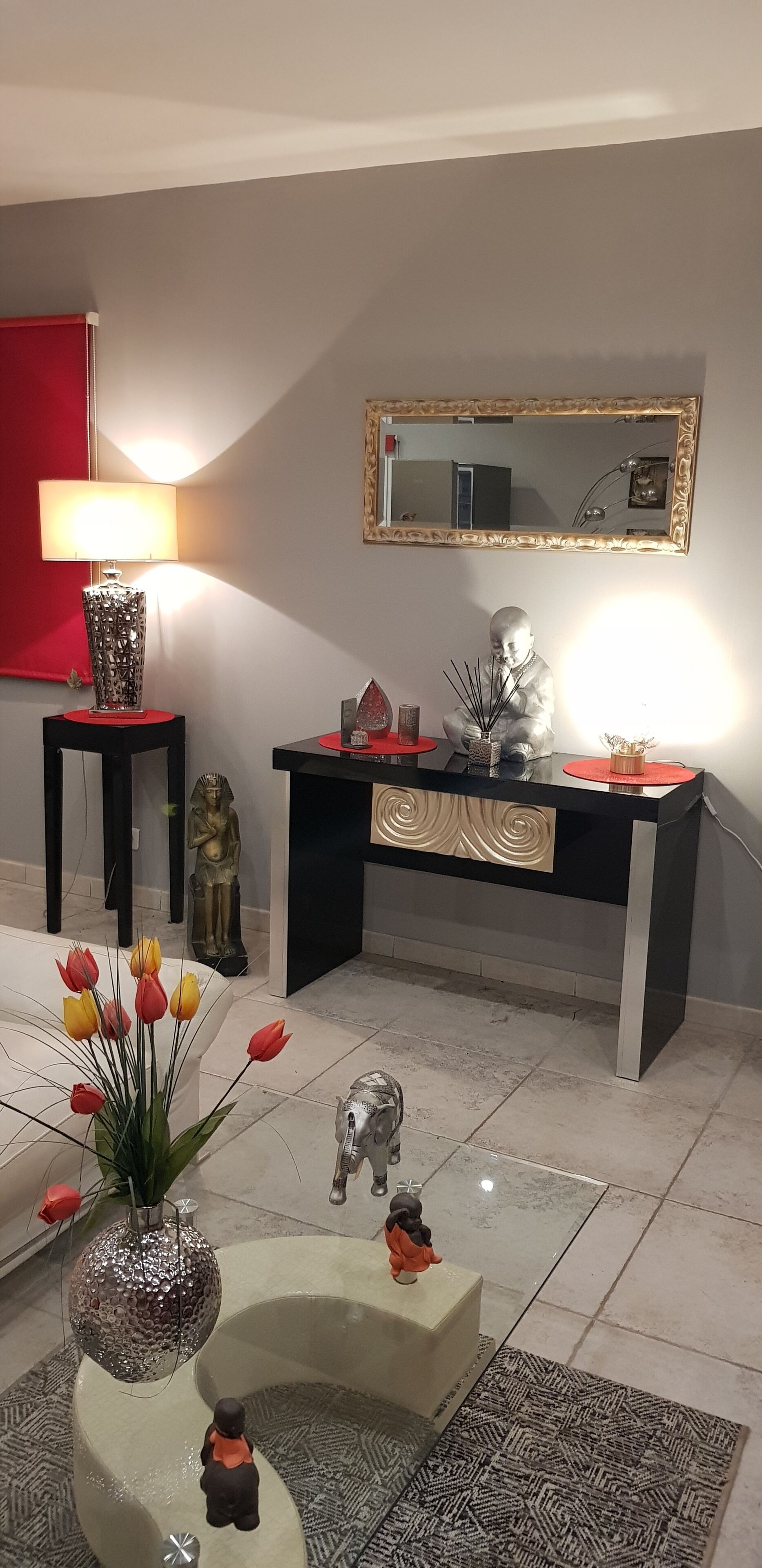 A modern living room with a black console table, a red accent wall, a large mirror, and decorative items including a vase of tulips and a small elephant figurine.