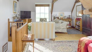 Un loft amplio con vigas de madera a la vista, un ventanal grande, un sofá, un televisor, una estantería y una escalera de madera.