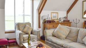 Una sala de estar acogedora con un sofá, una mesa de madera con una botella y vasos, y vistas al exterior.