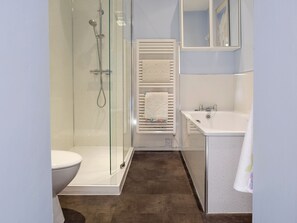 Un baño con ducha envuelta en vidrio, inodoro y lavamanos blancos, y un perchero con varias toallas.