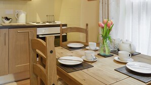 Cucina con mobili in legno, un fornello e un tavolo da pranzo apparecchiato con piatti, tazze e un vaso di tulipani.