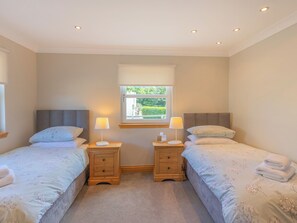 A twin bedroom with two beds, bedside tables, lamps, and a window with a view of greenery.