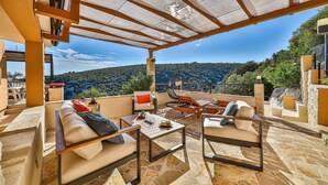 A covered outdoor seating area with a stone floor, a hanging chair, and a table with a candle. - Awesome home in Vinisce (Vinisce)