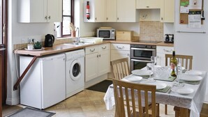 A compact kitchen with a washing machine, microwave, oven, and a dining area with a table set for two. - A characterful holiday home with an attractive open plan layout. (Lerryn)