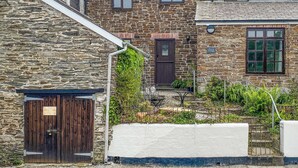 A stone cottage with a wooden door, a small garden, and a sign indicating 'Forth Cottage'. - A characterful holiday home with an attractive open plan layout. (Lerryn)
