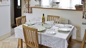 A dining table set for six with white lace tablecloths, wooden chairs, and a bottle of wine. - A characterful holiday home with an attractive open plan layout. (Lerryn)