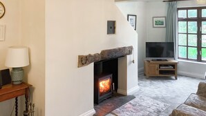 A living room with a fireplace, a television on a wooden stand, and a window with curtains. - A characterful holiday home with an attractive open plan layout. (Lerryn)