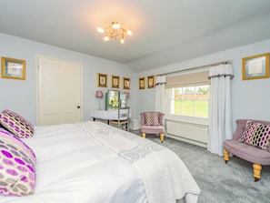 Um quarto com cama, uma cadeira, cômoda e janela com cortinas.