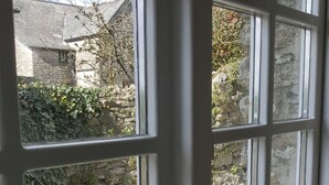Une vue à travers une fenêtre, avec des murs en pierre et un bâtiment en pierre en arrière-plan.