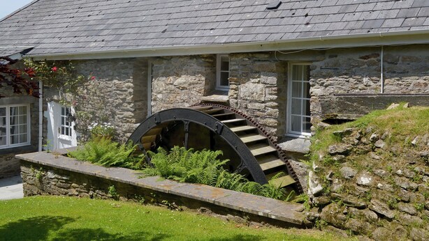 Un bâtiment en pierre doté d’une grande roue à eau et d’un escalier menant à une porte.
