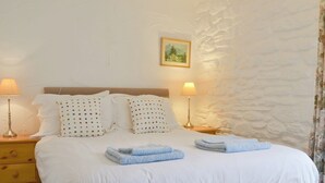 Un lit bien fait, avec du linge de lit blanc et des serviettes bleues, deux lampes de chevet et un tableau encadré au mur.