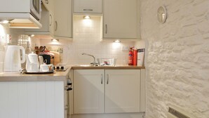 Une cuisine compacte avec des meubles blancs, un plan de travail en bois, un évier, une bouilloire et un extincteur.