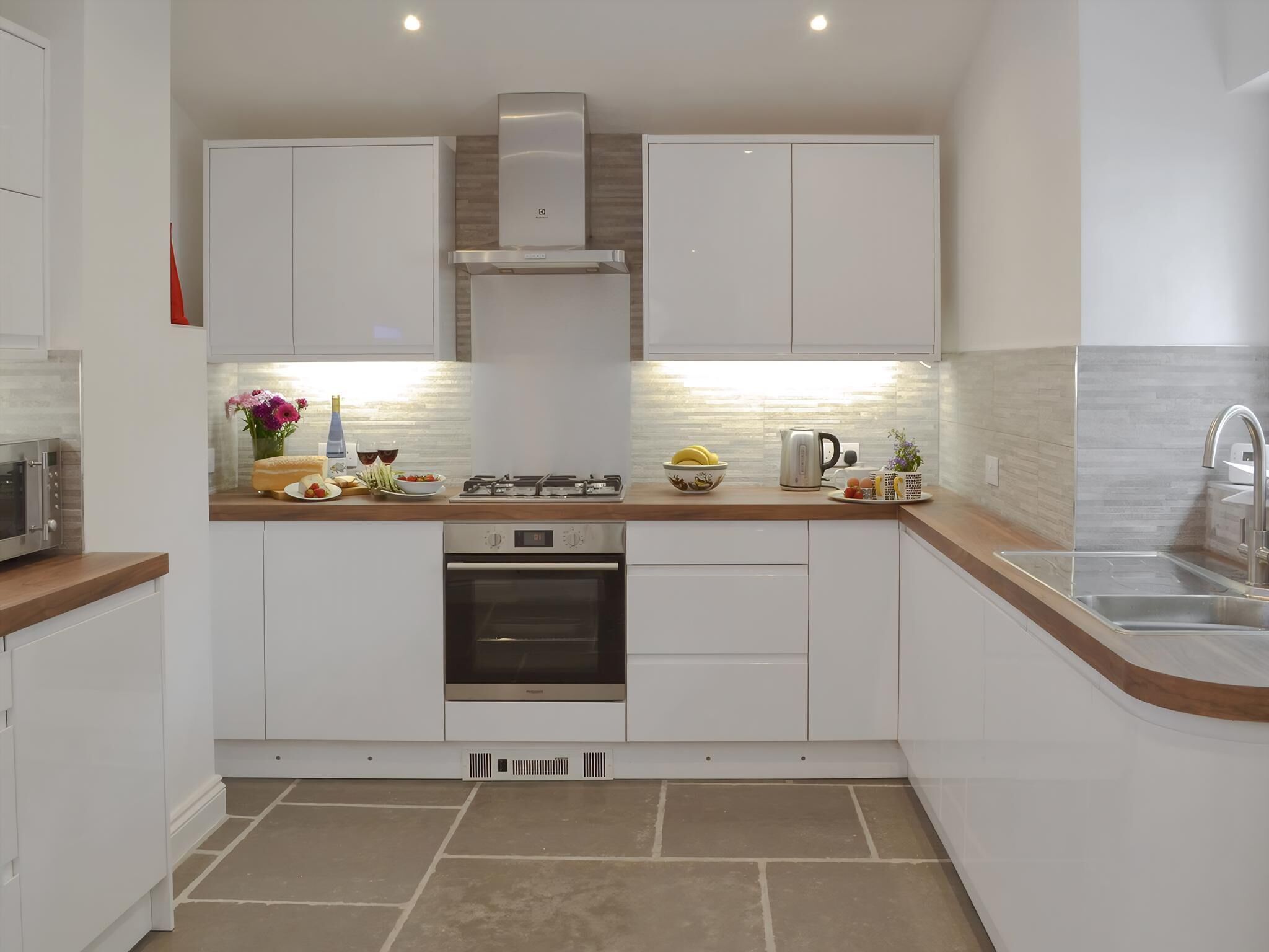 Una cucina moderna con mobili bianchi, una cappa aspirante in acciaio inossidabile, un forno integrato e un lavello con un rubinetto dal design contemporaneo.