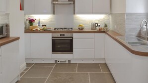 A modern kitchen with white cabinets, a stainless steel range hood, a built-in oven, and a sink with a modern faucet. - 2 bedroom accommodation in Brixham (Brixham)