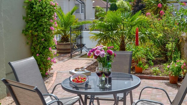 A patio with a round table, four chairs, a bowl of strawberries, two wine glasses, and a vase with flowers. - 2 bedroom accommodation in Brixham (Brixham)