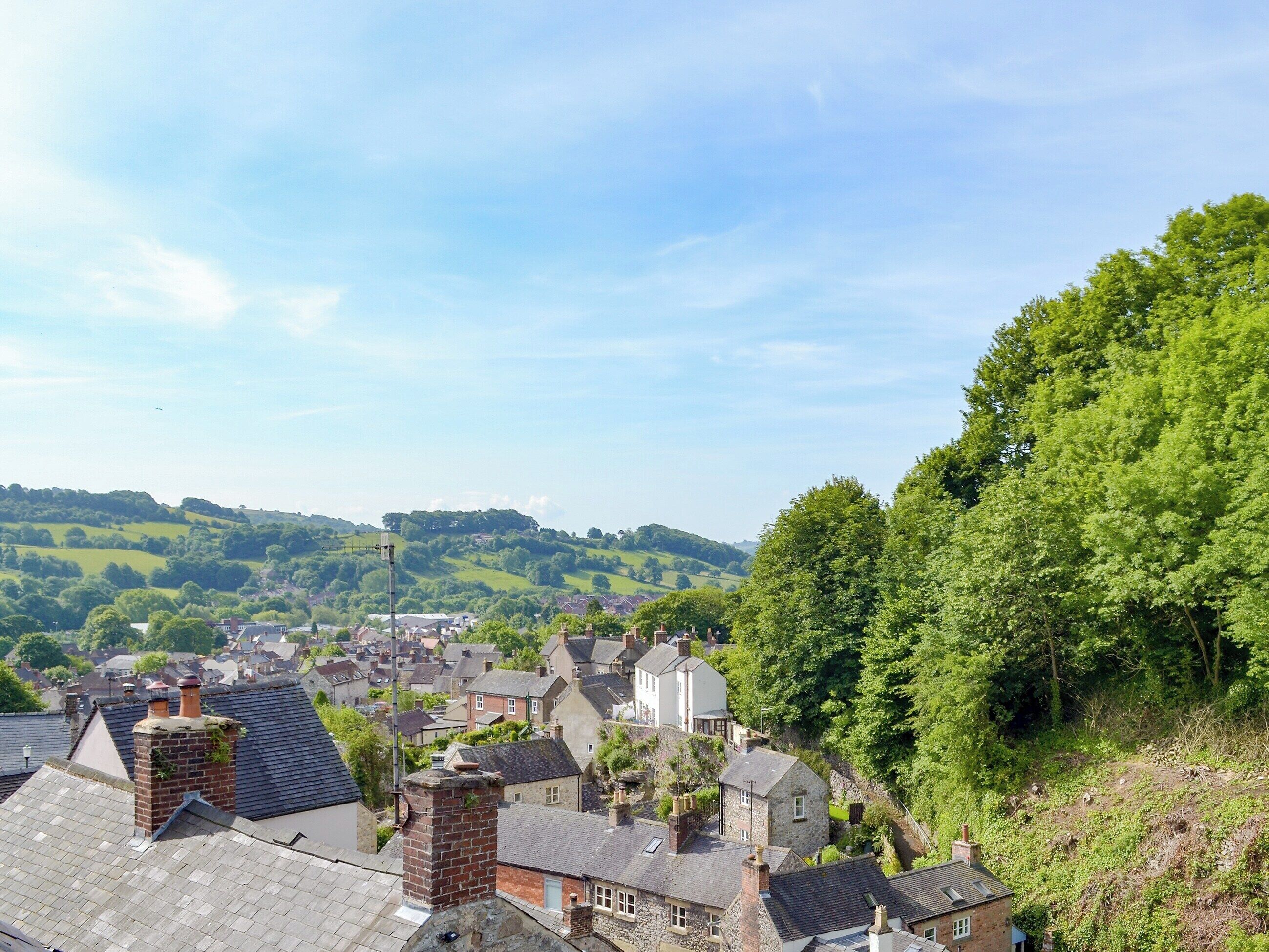 Une ville aux maisons traditionnelles, avec un imposant bâtiment blanc et, en arrière-plan, de luxuriantes collines verdoyantes.