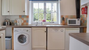 Une cuisine compacte équipée d’un lave-linge, d’un lave-vaisselle, d’un four à micro-ondes et d’une fenêtre donnant sur un espace verdoyant.