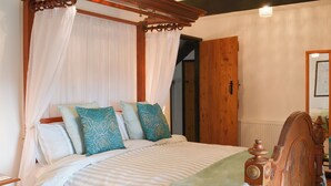 Un lit à baldaquin à quatre poteaux, avec une tête de lit en bois, une couvre-lit à rayures et des coussins décoratifs.