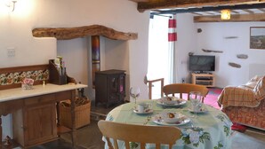 Un coin repas chaleureux avec une table dressée pour deux personnes, un banc en bois, une cheminée et un téléviseur en arrière-plan.