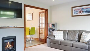 A living room with a fireplace, a grey sofa, a television, and a bookshelf. - 4 bedroom accommodation in Keswick (Keswick)