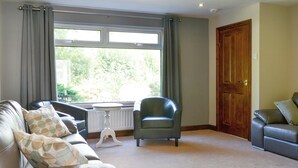 A living room with a sofa, a chair, a table, and a large window with curtains. - 4 bedroom accommodation in Keswick (Keswick)