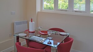 Zona pranzo con tavolo in vetro, sedie rosse, orologio a parete e finestra vista su vegetazione.