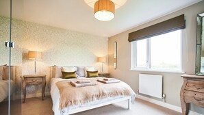 Ein Schlafzimmer mit einem Bett, Nachttischlampen, einem Fenster, einem Heizkörper und einer Kommode.
