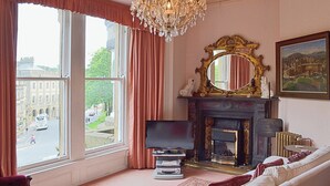 Ein Zimmer mit großem Fenster, Kamin, Fernseher und einer Couch.