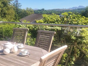 Een houten tafel met stoelen en theeservies op een balkon met uitzicht op een bergachtig landschap.