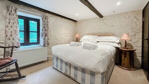 Un dormitorio con una cama grande, dos lámparas de noche, un sillón mecedora y una ventana con cortinas.