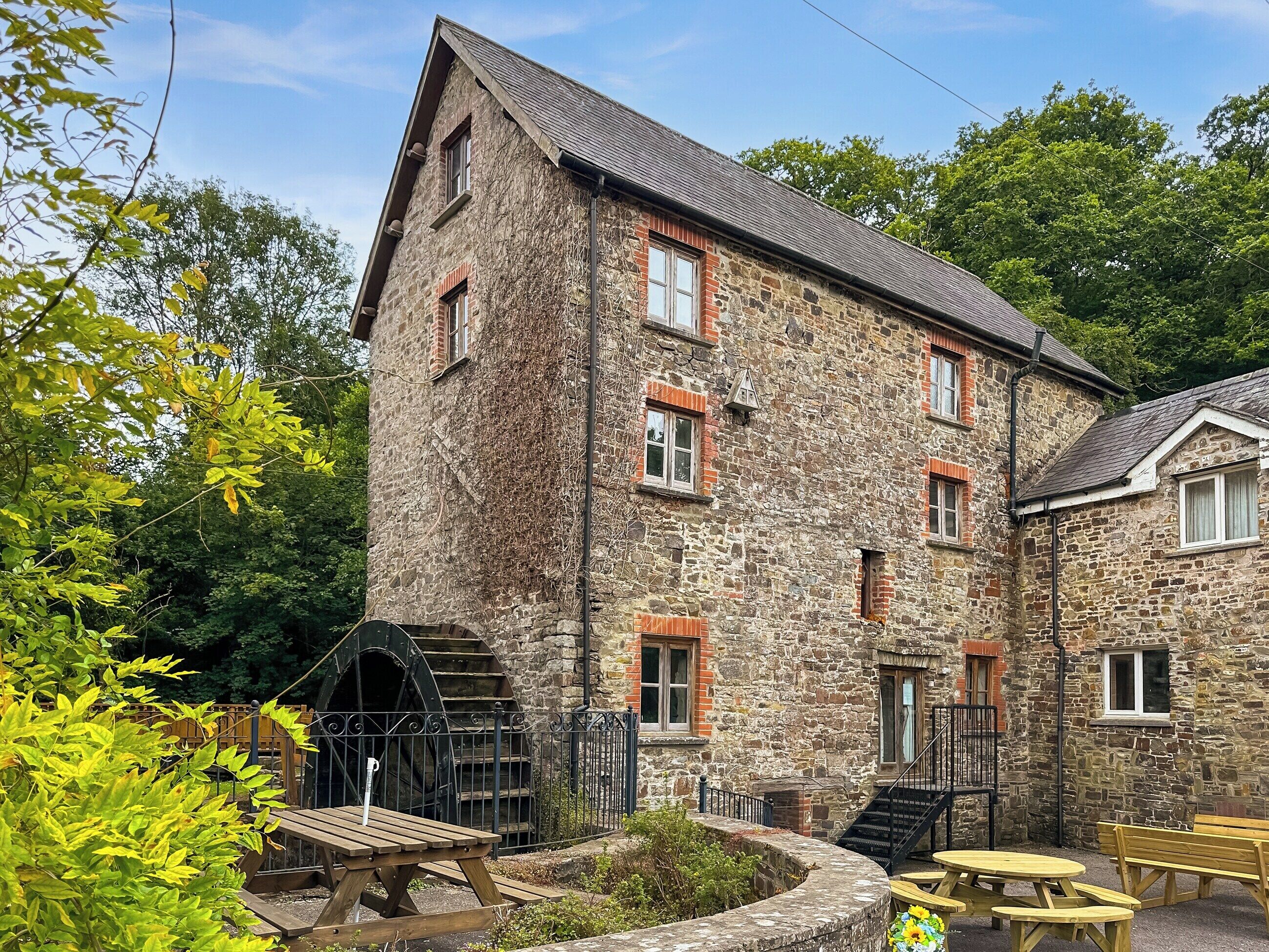 A stone building with a water wheel, wooden benches, and a staircase leading to the entrance.
