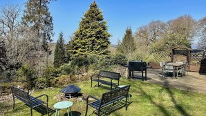 A backyard with a fire pit, a tall coniferous tree, a wooden pergola, and a barbecue area. - 3 bedroom accommodation in Beech Hill, near Bowness-on-Windermere (Beech Hill, near Bowness-on-Windermere)