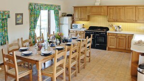 A kitchen with wooden cabinets, a dining table set for four, and a tiled floor. - 4 bedroom accommodation in Fairy Cross, Bideford (Fairy Cross, Bideford)